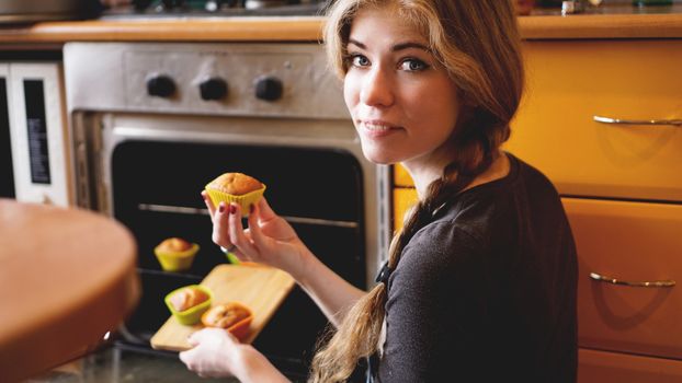 Beautiful blonde woman showing muffins in a kitchen. Cooking and home concept