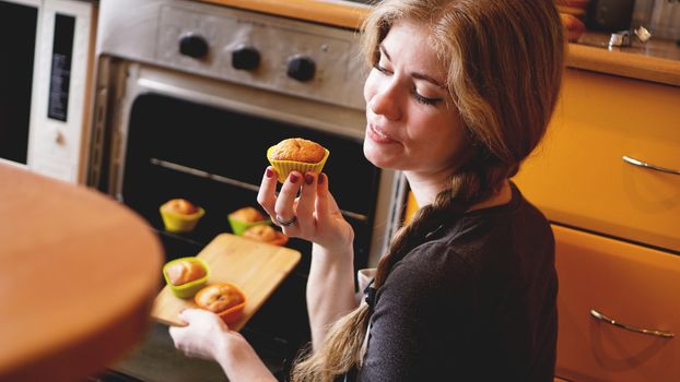 Beautiful blonde woman showing muffins in a kitchen. Cooking and home concept