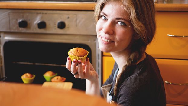 Beautiful blonde woman showing muffins in a kitchen. Cooking and home concept