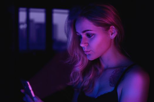 Girl using cellphone at night with neon light - pink and blue