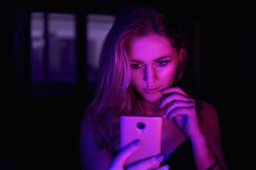 Girl using cellphone at night with neon light - pink and blue