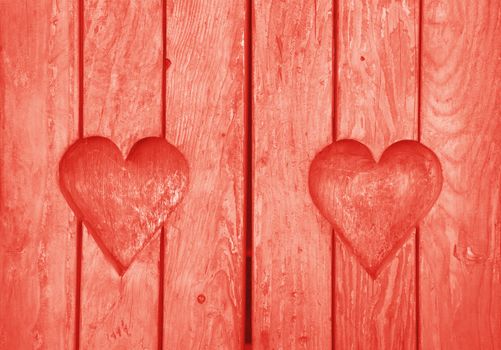 Close up two heart shaped elements, symbol of love, romance and togetherness, wood carved cut in wooden planks texture background, coral pink painted window shutter