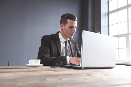 Young businessman in black suit using laptop in office