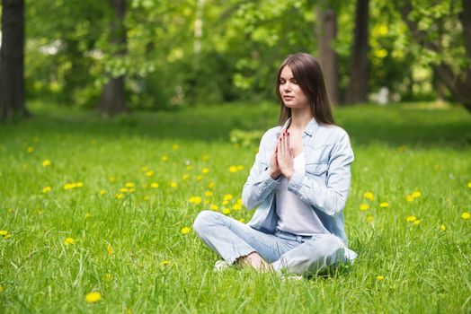 Beautiful young girl in casual clothes meditating in spring park