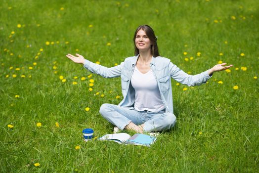 Beautiful young woman enjoy nature sitting in park with book and coffee