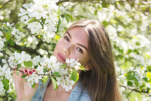 Beautiful young brunette woman standing near blooming apple tree