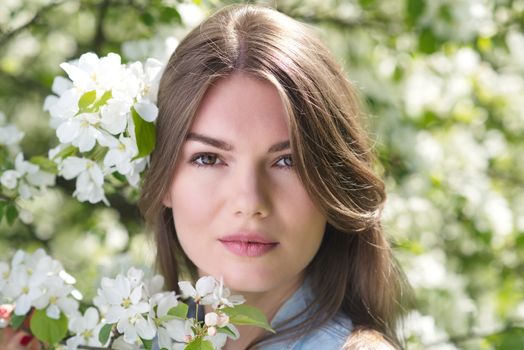 Beautiful young brunette woman standing near blooming apple tree