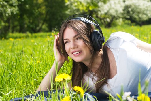 Young brunette woman with headphones listening to the music outdoors on sunny summer day