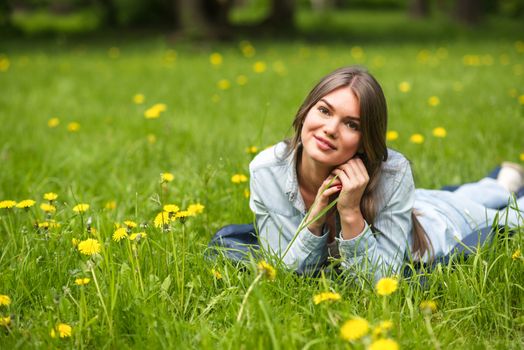 Beautiful young woman laying on grass with dandelion flowers in park