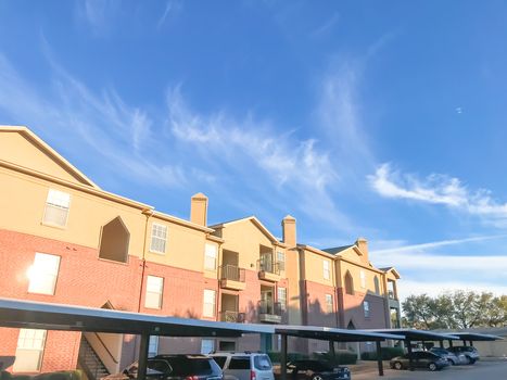 Apartment building complex and parked cars in Lewisville, Texas, USA. Low angle view of multi-stories rental real estate with covered parking at sunset with cloud sky