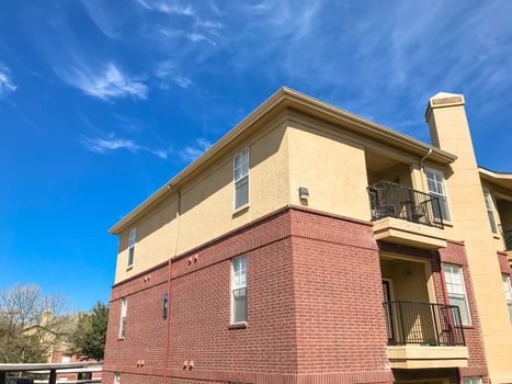 Lew angle view typical apartment building complex with covered parking in Lewisville, Texas, USA. Sunny spring day with blue sky and white clouds over tall chimney