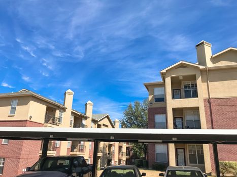 Lew angle view typical apartment building complex with covered parking in Lewisville, Texas, USA. Sunny spring day with blue sky and white clouds over tall chimney