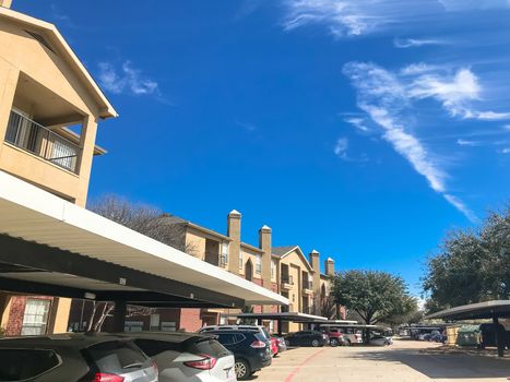 Lew angle view typical apartment building complex with covered parking in Lewisville, Texas, USA. Sunny spring day with blue sky and white clouds over tall chimney
