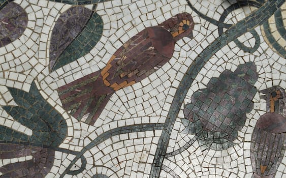 Mosaic picture of a bird sitting on a branch, made of ceramic tiles, top view.