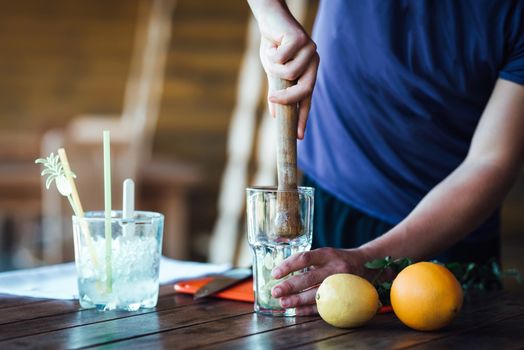 Barman prepares fruit alcohol cocktail based on lime, mint, orange, soda and alcohol