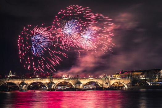A fireworks show is staged near the historical Charles Bridge in the centre of Prague, with reflections in water.