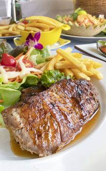 Grilled steak with french fries and fresh vegetables on white plate