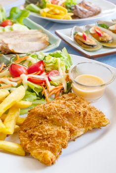 Deep fried fish steak served with french fries and fresh vegetables on plate , And  full of food on table