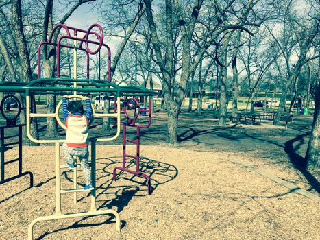 Healthy Asian toddler boy climbing structure at outdoor playground in Lewisville, Texas, USA. Sunny day of wintertime in North Texas