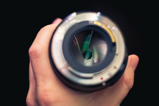DSLR lens in hand with partly closed aperure, visible aperture blades. Lens in hand.