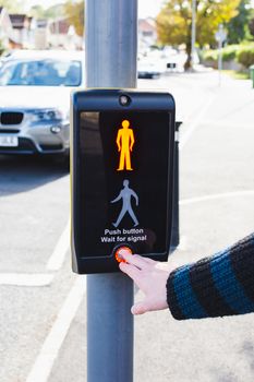 man pushing a button on a pedestrian traffic light, car waiting in the background