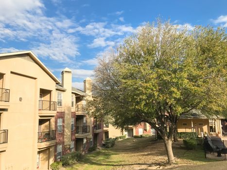 Apartment building complex with steep backyard and oak trees in suburban Dallas, Texas, USA. Low angle view of multi-stories rental real estate with covered parking at sunset cloud sky