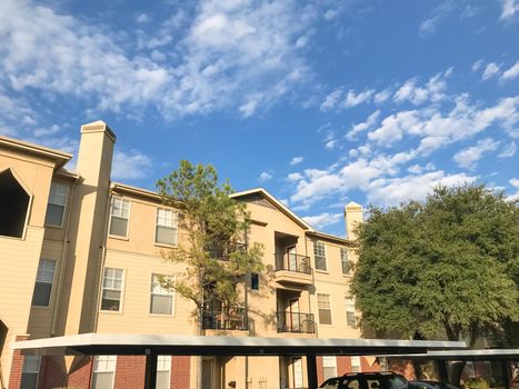 Typical multistory apartment building complex in suburban Dallas, Texas, USA. Low angle view of multi-stories rental real estate with covered parking at sunset with cloud sky