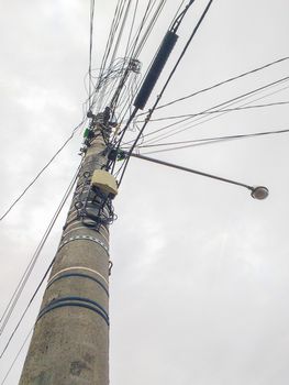 Silhouette of Cement post with excess electric wires, and lamp with cloudy sky in the background