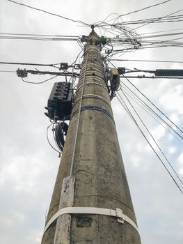 Silhouette of cement pole with excess electric wires, cloudy sky in the background