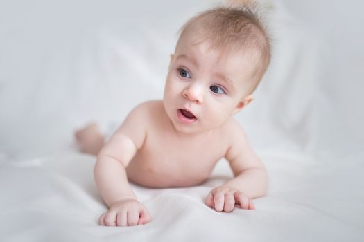 Amazed baby boy relaxing in bed on white