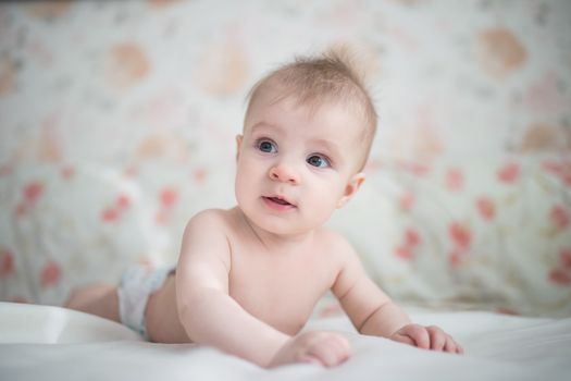 Curious baby boy lying in bed on white