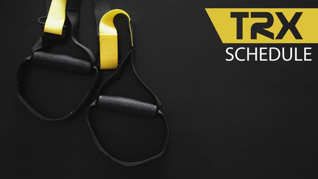 Black and yellow strap functional training equipment on grey background. Sport accessories. Fitness and Gym workout items. Banner TRX SCHEDULE
