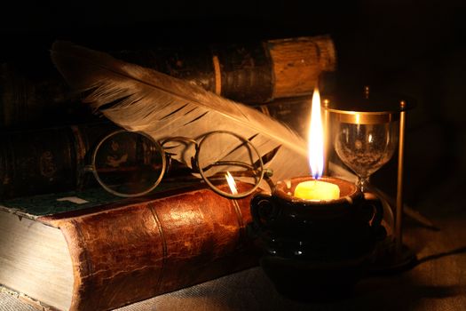 Old books and quill pen near lighting candle on dark background