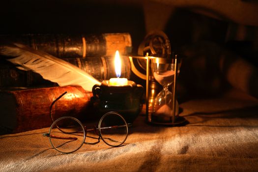 Vintage still life with old glasses against lighting candle and books