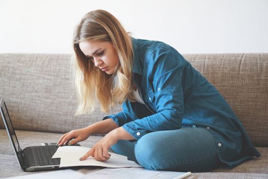 Serious woman focused on finding information on paper. Sitting at home in front of a laptop. The concept of business and online student learning