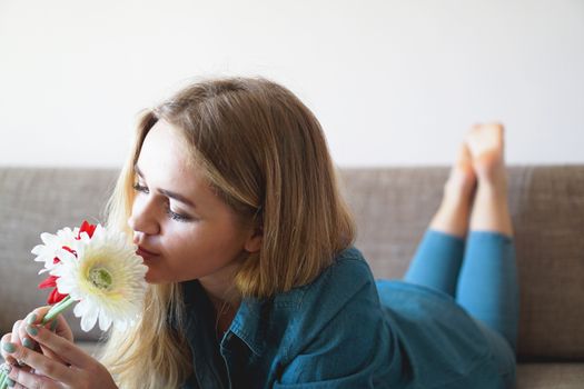 Attractive young woman sniffing bouquet of flowers lying on the couch