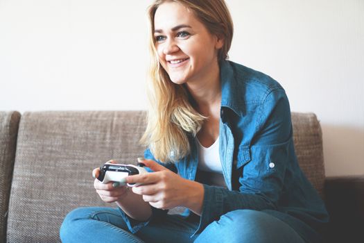 Girl gamer plays with a wireless gamepad while looking at the screen in front of her. Young blonde girl smiles and enjoys playing video games console.