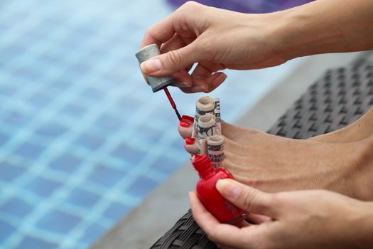 Woman painting nails using dollar bills sitting outdoors by the pool