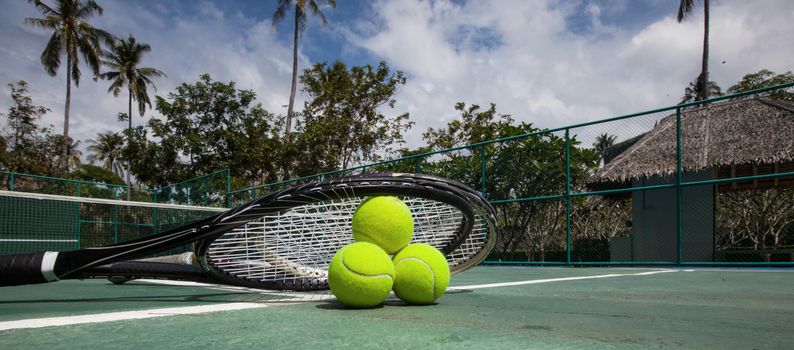 Tennis balls and racket in outdoor tropical court