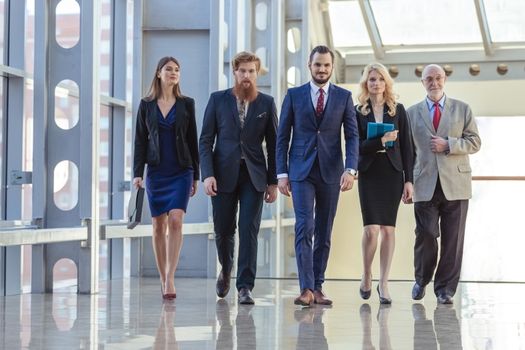 Full length of group of happy young business people walking the corridor in office together