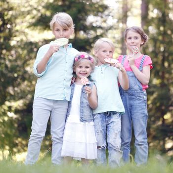 Group of happy children eating lollipops outdoors in summer park