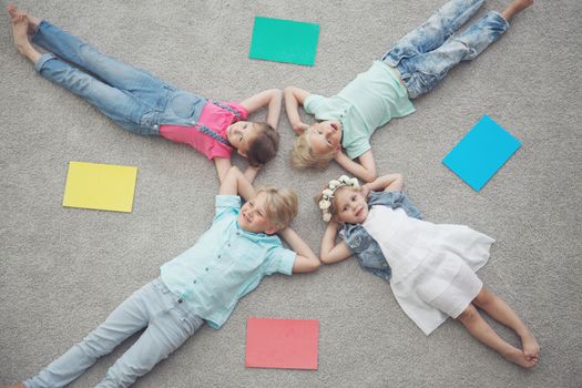 Four happy children laying on floor and smiling among colorful paper