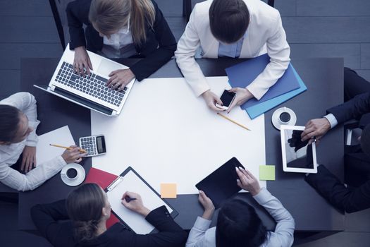 Business workplace with people, cup of coffee, digital tablet, smartphone, papers and various office objects on table