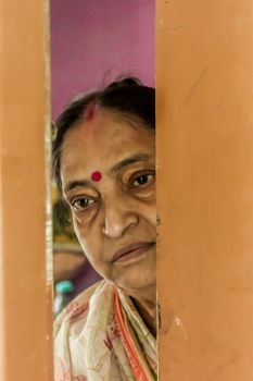 Thoughtful, sad, Worried and alone elderly senior woman peeping through the door at home and eagerly waiting for her son to come. Loneliness concept