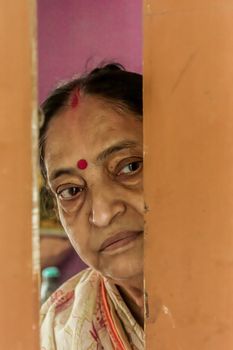 Thoughtful, sad, Worried and alone elderly senior woman peeping through the door at home and eagerly waiting for her son to come. Loneliness concept