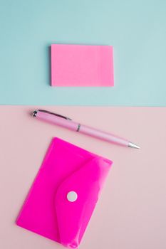 Creative vertical flat lay, top view office Desk. Workspace with space for text, Notepad, pen, plastic envelope stationery for women blogger, freelancer on pink and blue background