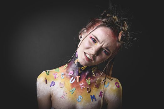 Emotional portrait of a young girl with creative makeup and colorful letters on her shoulders