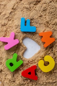 Heart shape and colorful Letters made of wood on sand