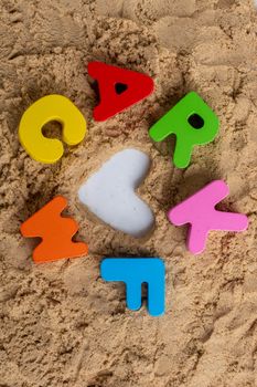 Heart shape and colorful Letters made of wood on sand