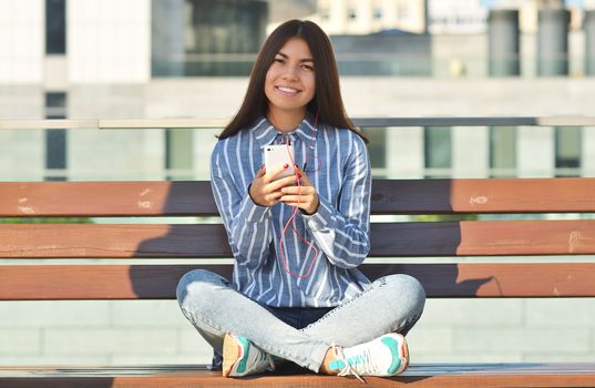 Young beautiful is asian girl sitts on the bench and listen to music. Spring sunny day